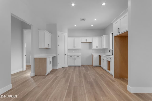 kitchen with dishwashing machine, light hardwood / wood-style floors, sink, and white cabinets