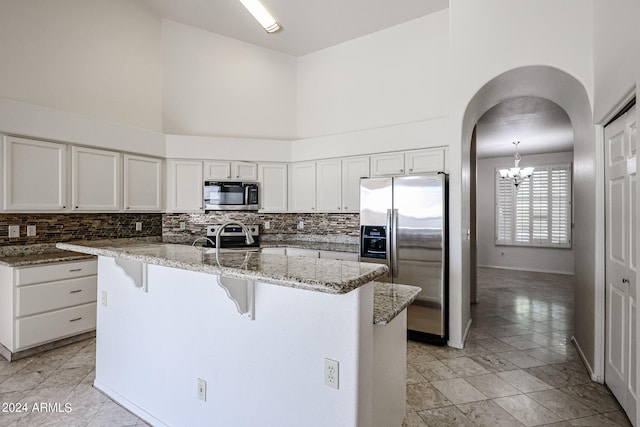 kitchen with appliances with stainless steel finishes, a high ceiling, stone counters, and a breakfast bar area