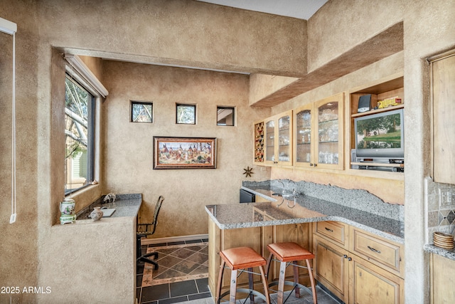 interior space with a kitchen breakfast bar, light brown cabinets, light stone countertops, and kitchen peninsula