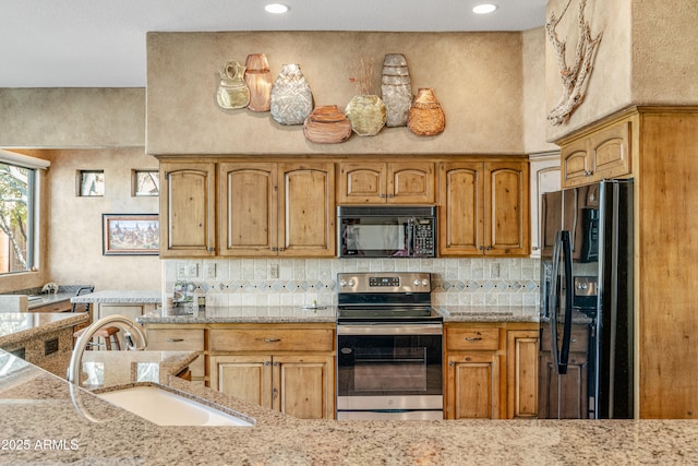 kitchen with black appliances, light stone counters, sink, and a high ceiling