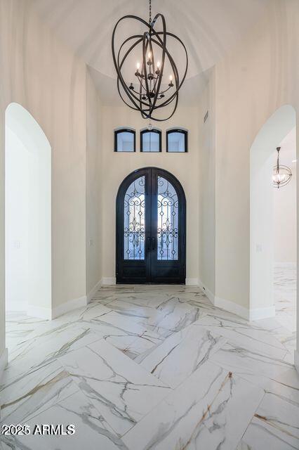 entrance foyer featuring arched walkways, a notable chandelier, and french doors