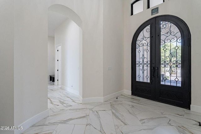 foyer entrance featuring marble finish floor, baseboards, arched walkways, and french doors