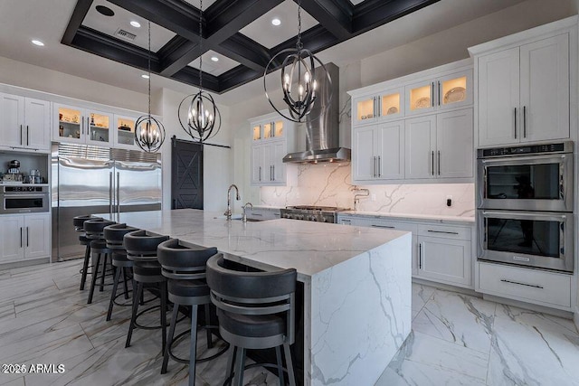 kitchen featuring wall chimney exhaust hood, a center island with sink, white cabinetry, and stainless steel appliances