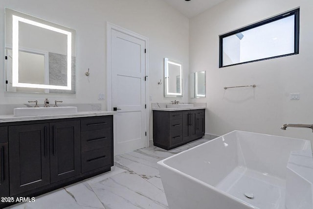 bathroom with marble finish floor, two vanities, a soaking tub, and a sink