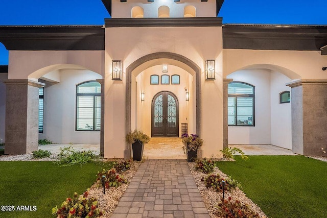 view of exterior entry with french doors, a lawn, and stucco siding