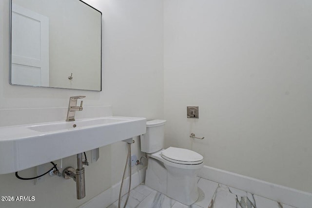 half bathroom featuring marble finish floor, baseboards, and toilet