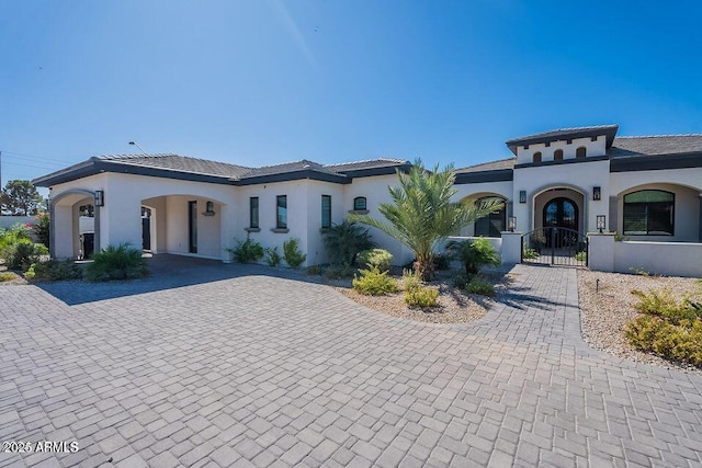 mediterranean / spanish-style house featuring a fenced front yard, decorative driveway, stucco siding, and a gate