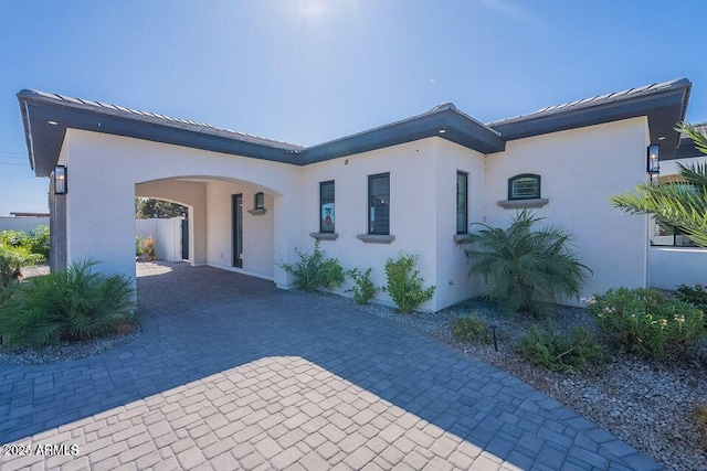 back of house featuring metal roof, decorative driveway, and stucco siding