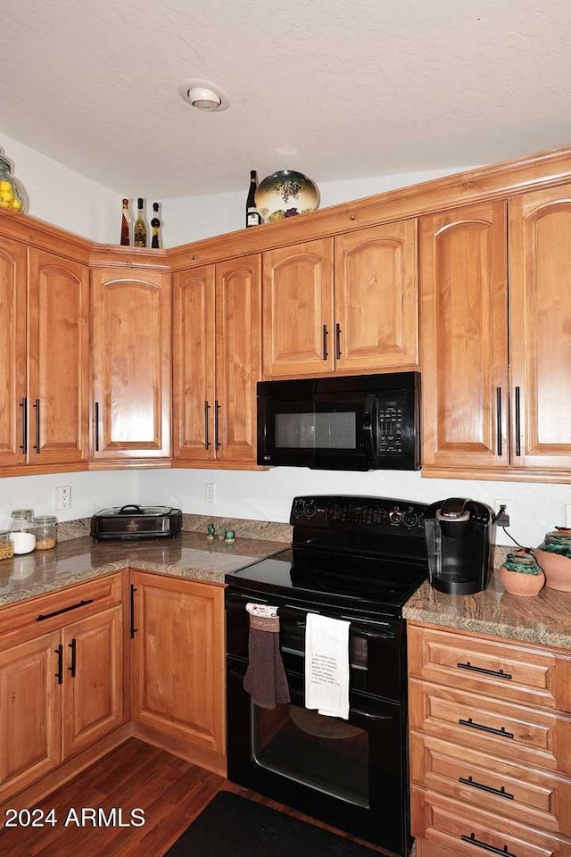 kitchen featuring dark hardwood / wood-style floors, vaulted ceiling, dark stone countertops, and black appliances