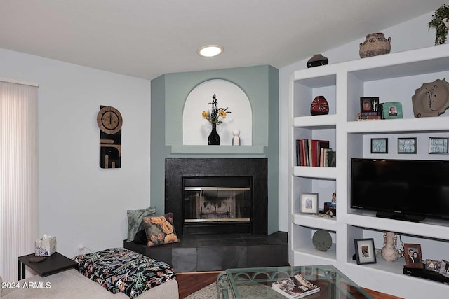 living room featuring built in shelves, hardwood / wood-style flooring, vaulted ceiling, and a tiled fireplace