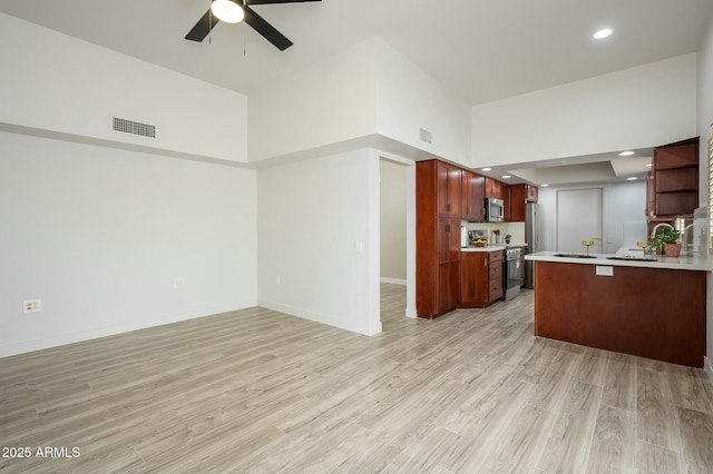 kitchen with appliances with stainless steel finishes, a high ceiling, ceiling fan, kitchen peninsula, and light wood-type flooring