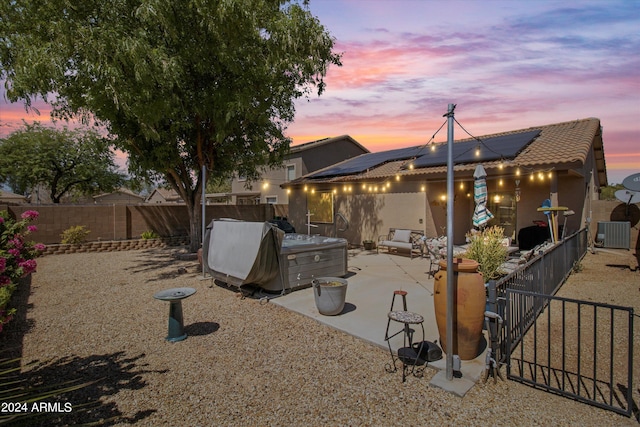 back house at dusk featuring cooling unit, solar panels, a patio area, and a hot tub