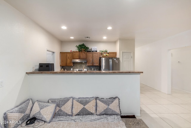 kitchen featuring tasteful backsplash, light tile patterned floors, kitchen peninsula, and stainless steel fridge