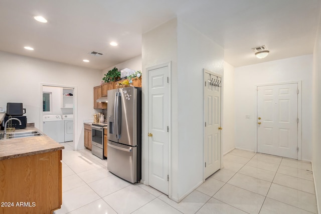 kitchen with washing machine and dryer, light tile patterned floors, appliances with stainless steel finishes, and sink