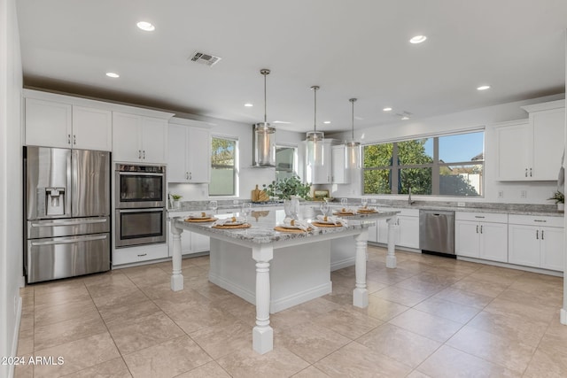 kitchen with appliances with stainless steel finishes, wall chimney exhaust hood, decorative light fixtures, white cabinets, and a kitchen island