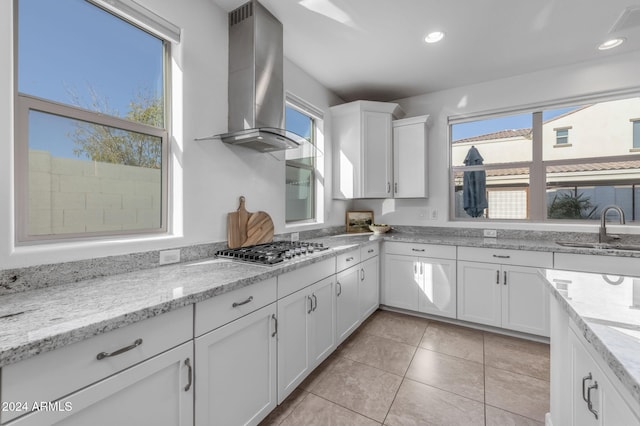 kitchen featuring light stone countertops, stainless steel gas cooktop, sink, wall chimney range hood, and white cabinets