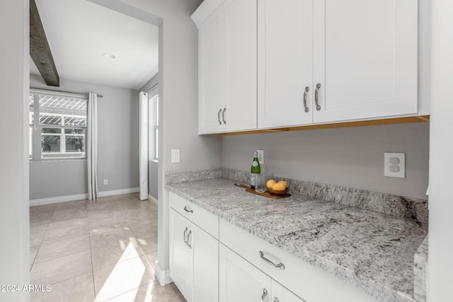 kitchen with white cabinets, light stone countertops, beamed ceiling, and light tile patterned floors