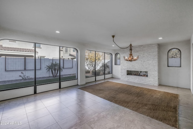 unfurnished living room with a stone fireplace, light tile patterned floors, and an inviting chandelier