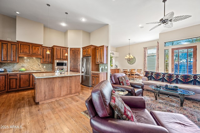 kitchen featuring light stone counters, decorative light fixtures, light wood-type flooring, a kitchen island, and stainless steel appliances