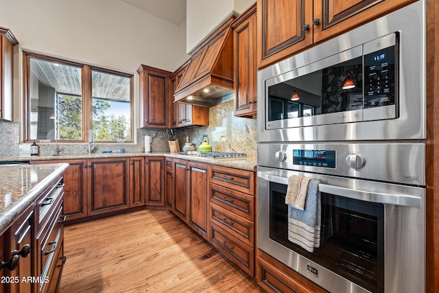 kitchen with tasteful backsplash, light hardwood / wood-style flooring, light stone countertops, and appliances with stainless steel finishes