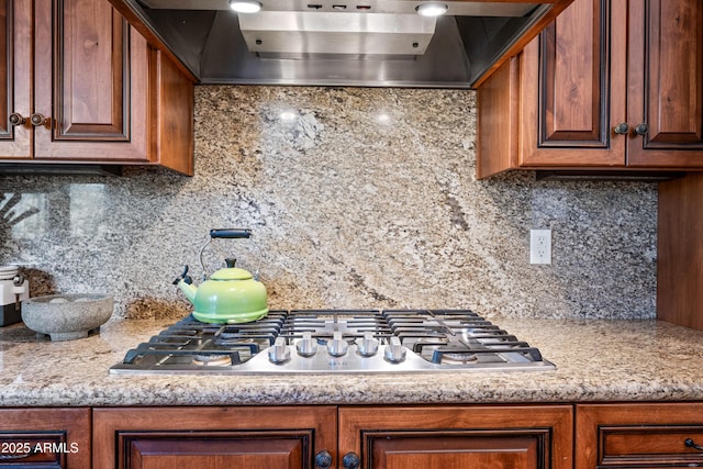 kitchen with stainless steel gas cooktop, backsplash, light stone counters, and wall chimney exhaust hood