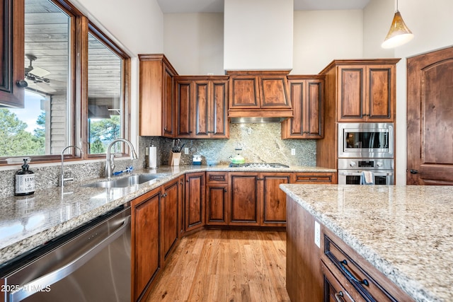 kitchen featuring tasteful backsplash, sink, hanging light fixtures, stainless steel appliances, and light hardwood / wood-style flooring