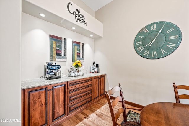 bar with light stone counters and light hardwood / wood-style floors