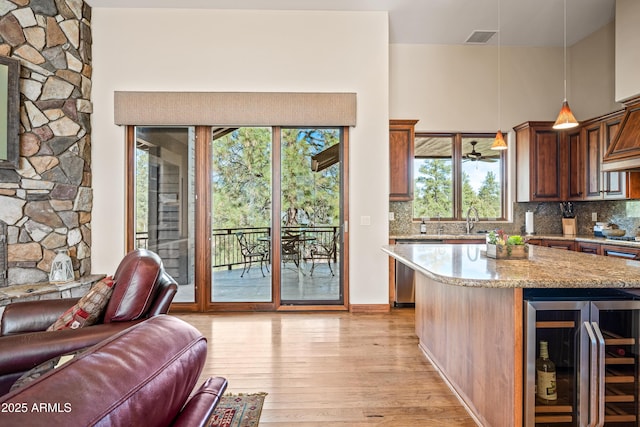 kitchen with wine cooler, decorative light fixtures, light hardwood / wood-style flooring, stainless steel dishwasher, and light stone countertops