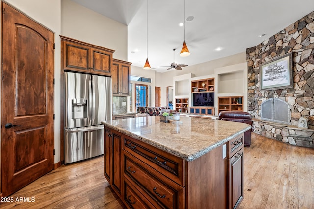 kitchen featuring pendant lighting, stainless steel fridge, light hardwood / wood-style flooring, a center island, and a stone fireplace