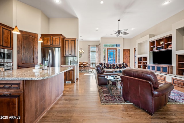 kitchen featuring appliances with stainless steel finishes, pendant lighting, ceiling fan with notable chandelier, light hardwood / wood-style floors, and light stone countertops