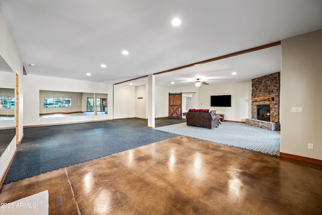 unfurnished living room with a stone fireplace, concrete flooring, a barn door, and ceiling fan