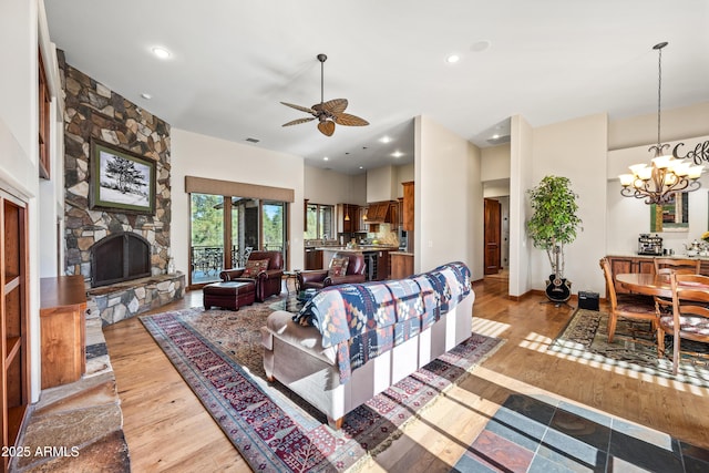 living room with ceiling fan with notable chandelier, a fireplace, and light hardwood / wood-style floors