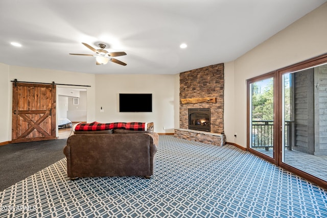 living room featuring ceiling fan, carpet flooring, a barn door, and a stone fireplace