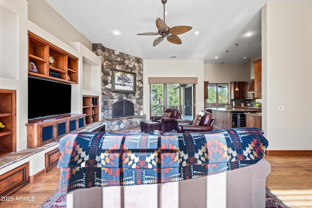 living room with a fireplace, beverage cooler, ceiling fan, and light wood-type flooring