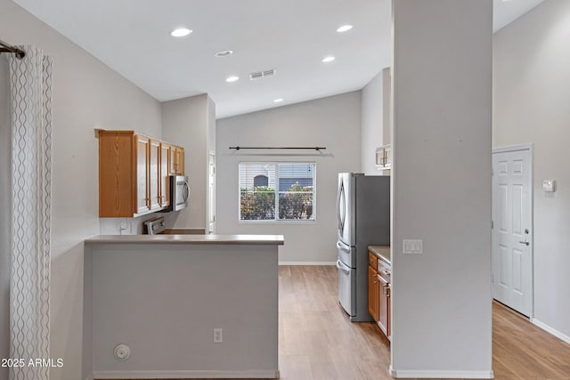 kitchen featuring brown cabinetry, visible vents, vaulted ceiling, light wood finished floors, and stainless steel appliances