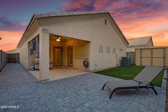 back of property at dusk featuring a storage shed, central AC unit, a fenced backyard, and a patio area