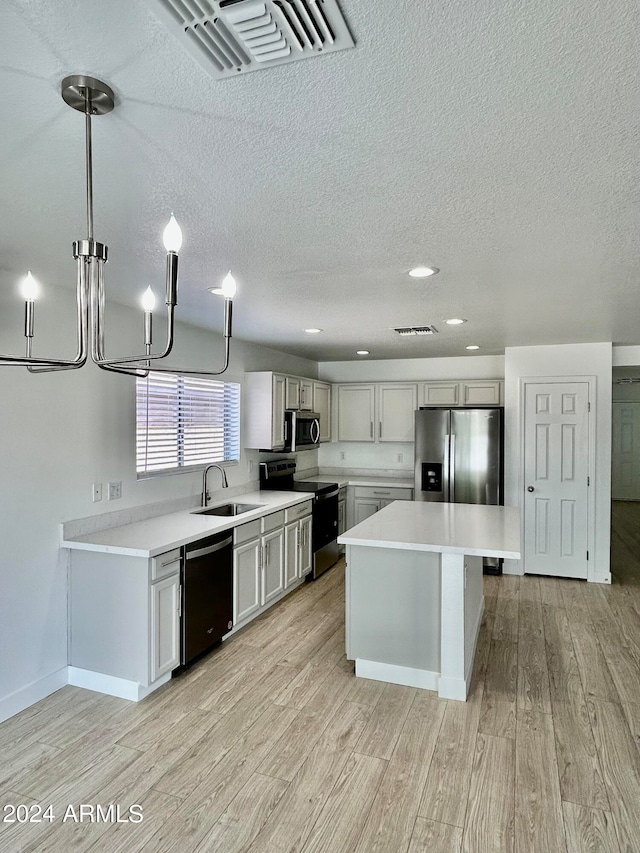 kitchen with sink, a center island, decorative light fixtures, black appliances, and light wood-type flooring