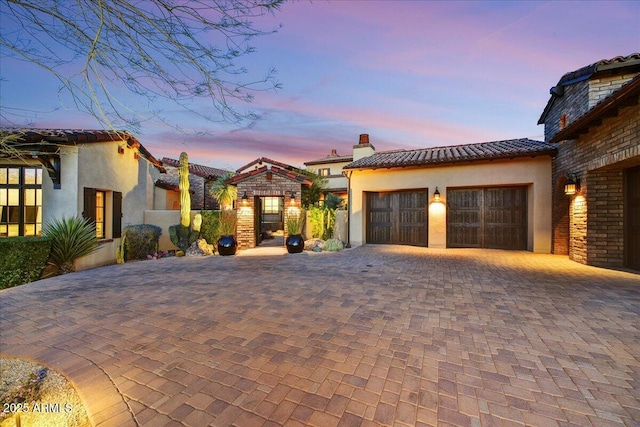 mediterranean / spanish-style house with stucco siding, decorative driveway, an attached garage, a chimney, and a tiled roof