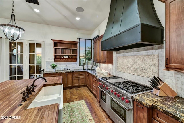 kitchen featuring custom exhaust hood, range with two ovens, open shelves, dark wood-style flooring, and decorative backsplash