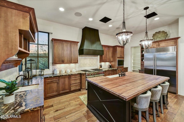 kitchen with decorative backsplash, premium range hood, built in appliances, and a sink