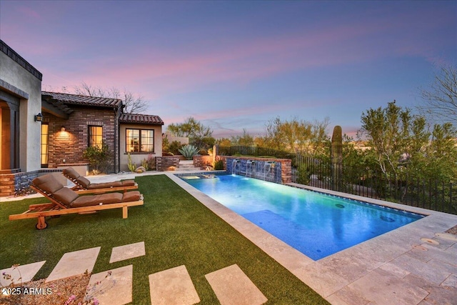 pool at dusk with a lawn, a fenced in pool, and fence