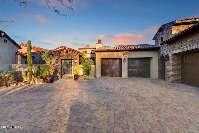 view of front of property with fence, a tiled roof, stucco siding, decorative driveway, and an attached garage