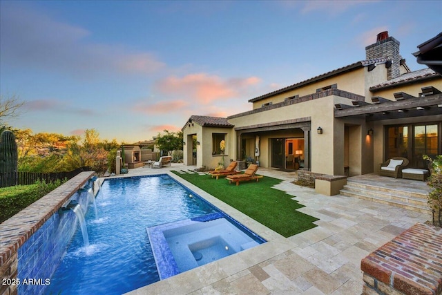 back of property at dusk featuring stucco siding, a tile roof, a pool with connected hot tub, fence, and a patio area