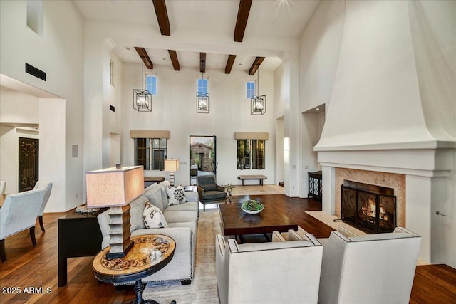 living area featuring a towering ceiling, beam ceiling, hardwood / wood-style floors, and a fireplace