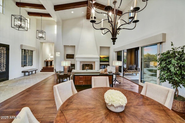 dining room with dark wood-type flooring, a towering ceiling, beamed ceiling, a chandelier, and a large fireplace