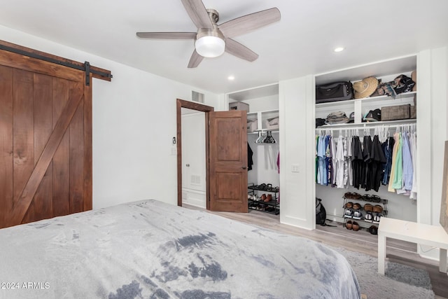 bedroom with ceiling fan, a barn door, and light wood-type flooring