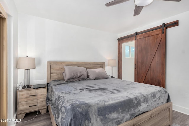 bedroom featuring dark hardwood / wood-style flooring, a barn door, and ceiling fan