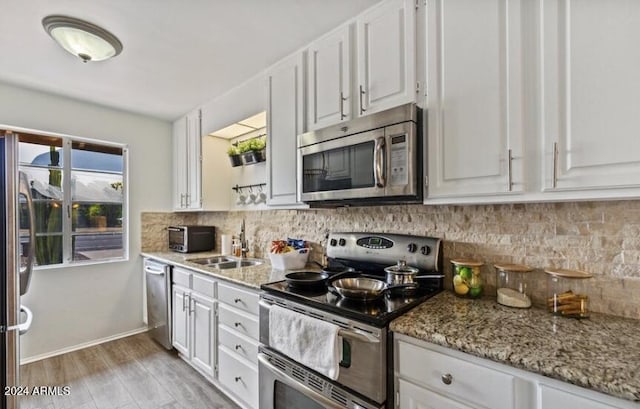 kitchen with sink, light wood-type flooring, light stone counters, white cabinetry, and stainless steel appliances