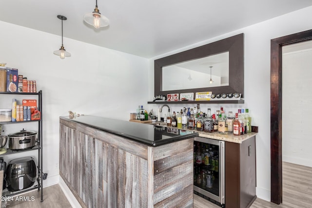 bar with pendant lighting, light hardwood / wood-style floors, sink, and beverage cooler