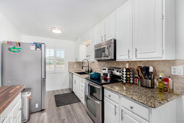 kitchen featuring appliances with stainless steel finishes, light wood-type flooring, dark stone counters, sink, and white cabinetry